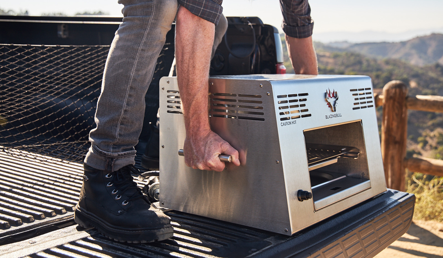 Man holding side handles of portable Blazing Bull Grill
